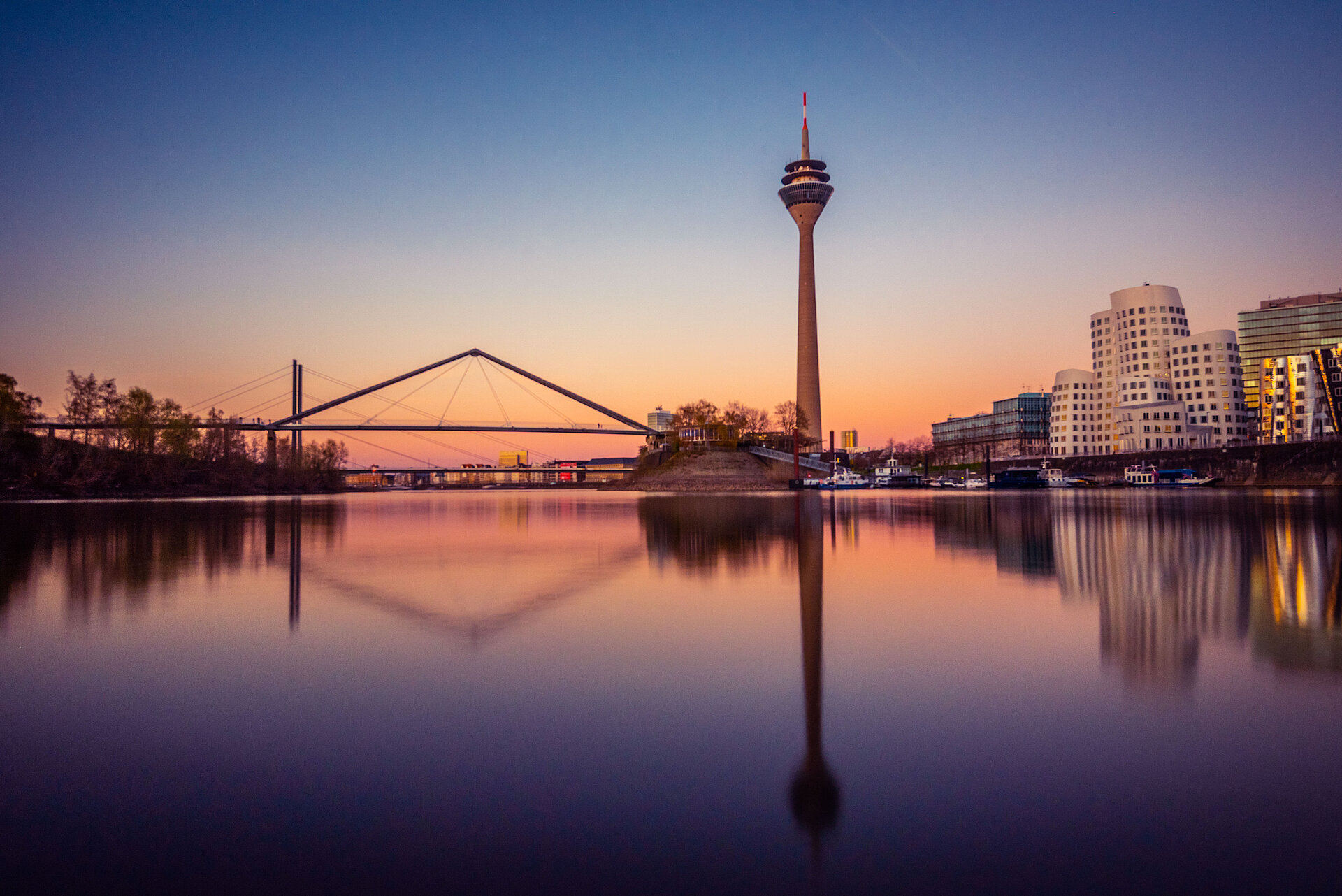 Düsseldorfer Skyline bei Dämmerung mit dem Rheinturm und seiner Spiegelung im Rhein.