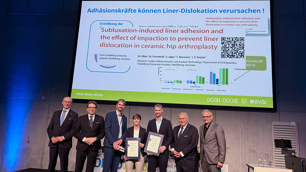 Award recipients and presenters on stage at DKOU 2026 beneath a slide on ceramic hip arthroplasty liner adhesion.
