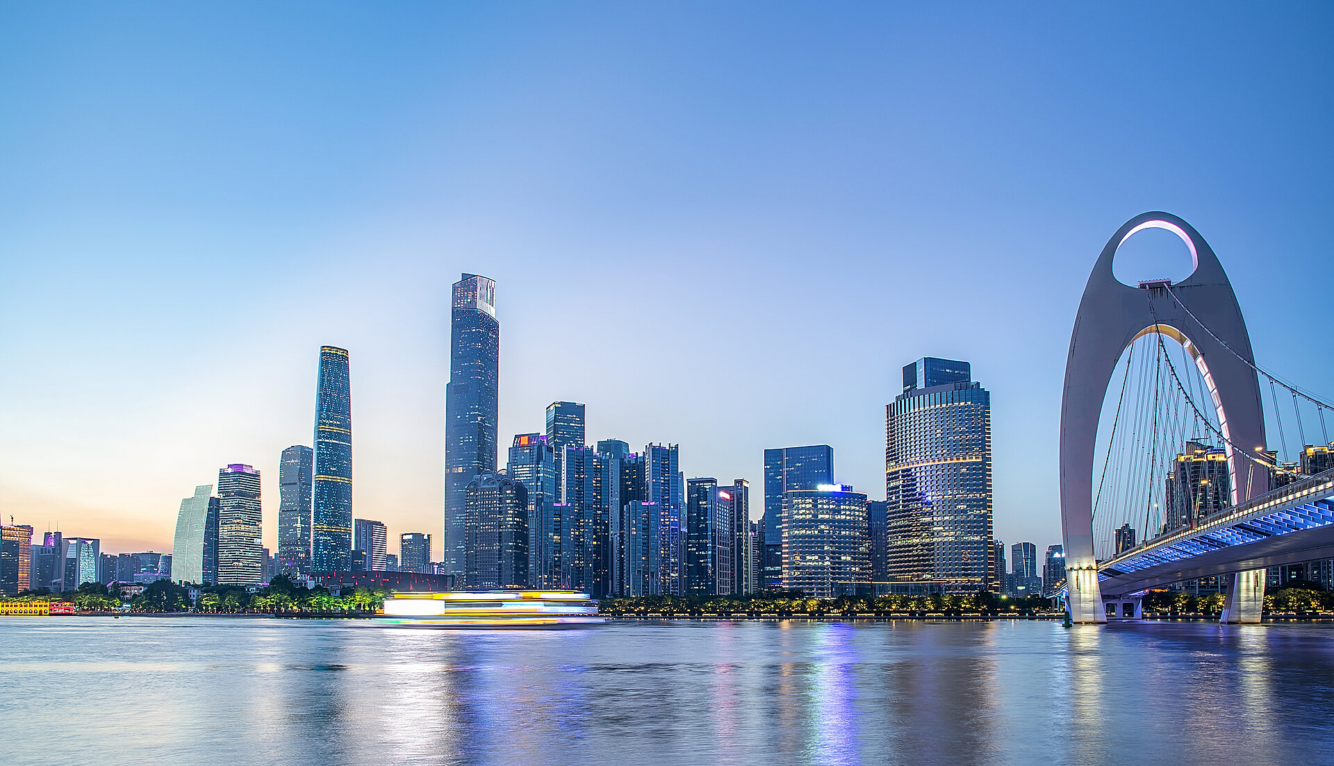 Skyline von Guangzhou bei Dämmerung mit Hochhäusern und beleuchteter Brücke am Fluss.