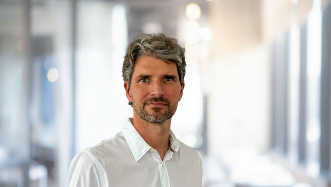 Alessandro Alan Porporati in a white shirt in front of a bright, softly blurred office corridor