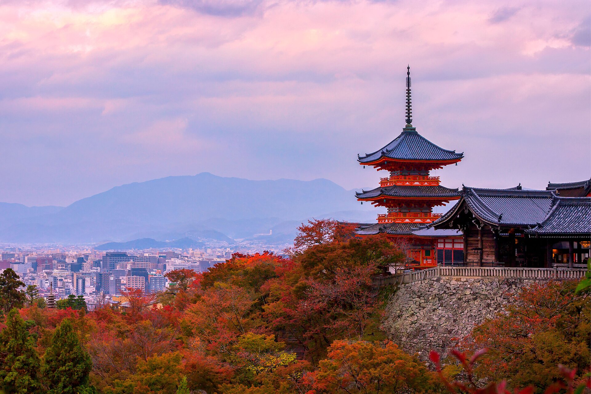 Kyoto-Tempel mit Blick auf die Stadt und Herbstlaub unter rosa Himmel.