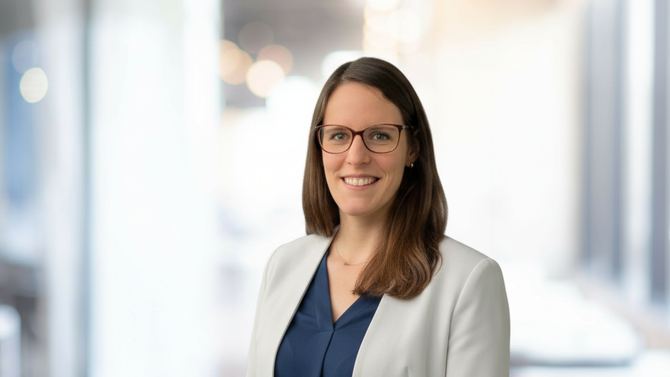 Yvonne Mödinger in a white blazer and dark blue blouse in front of a bright office corridor